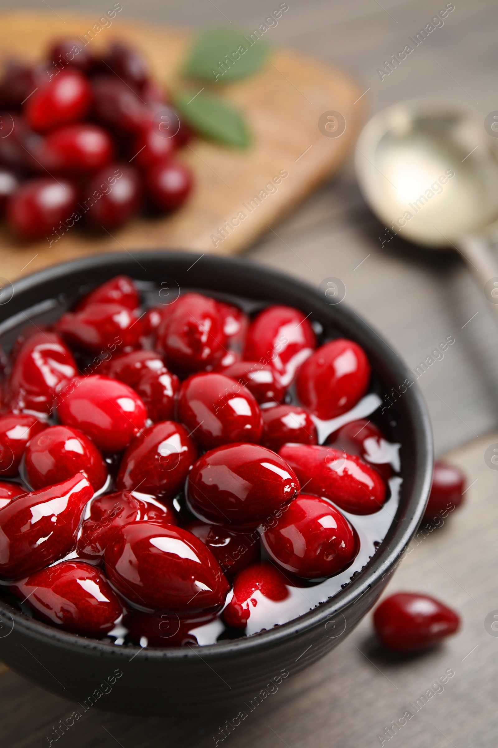 Photo of Delicious dogwood jam with berries in bowl on wooden table, closeup