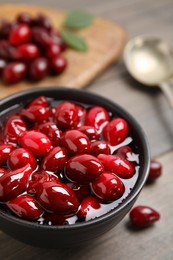 Photo of Delicious dogwood jam with berries in bowl on wooden table, closeup