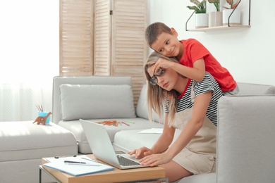 Photo of Little boy bothering mother at work in living room. Home office concept