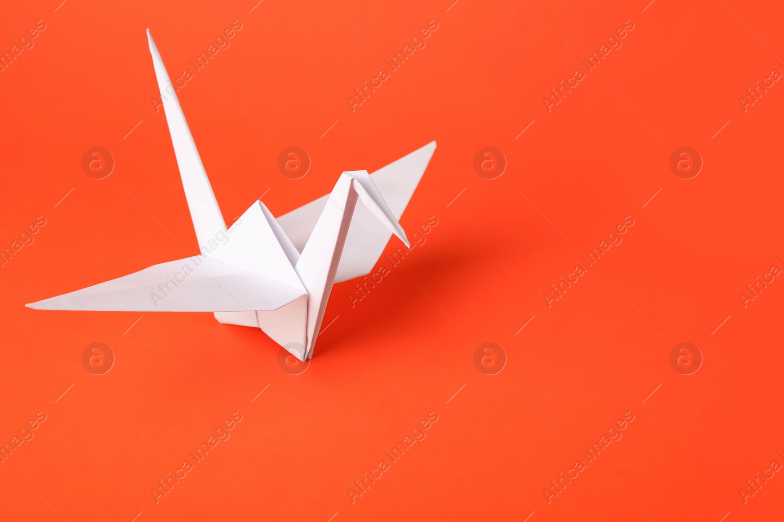 Photo of Origami art. Handmade paper crane on orange background, space for text