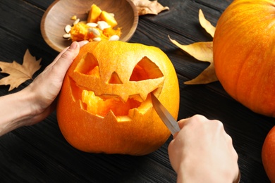 Photo of Woman carving Halloween pumpkin head jack lantern on wooden table, closeup