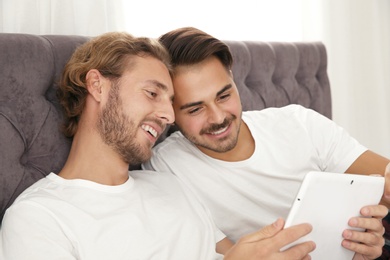Happy gay couple with tablet computer on bed at home