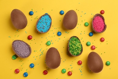 Sweet chocolate eggs with sprinkles and candies on yellow background, flat lay