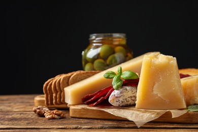 Photo of Delicious parmesan cheese, sausage, olives and basil on wooden table