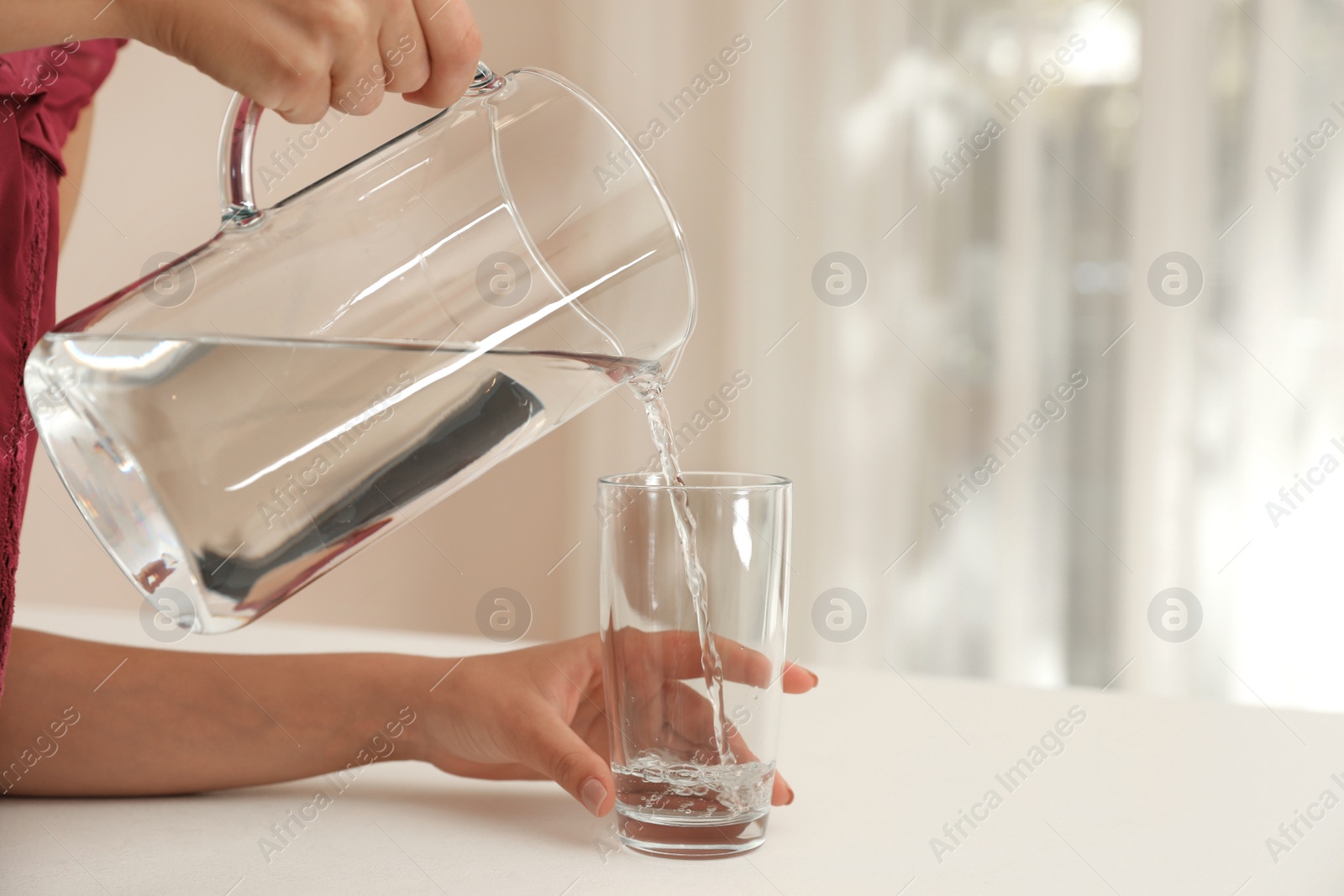 Photo of Woman pouring water from jug into glass indoors, closeup. Space for text