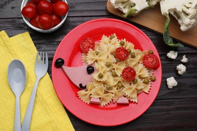 Photo of Creative serving for kids. Plate with cute hedgehog made of delicious pasta, sausages and tomatoes on black wooden table, flat lay