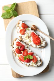 Photo of Delicious ricotta bruschettas with strawberry, mint and pistachios served with honey on white wooden table, flat lay