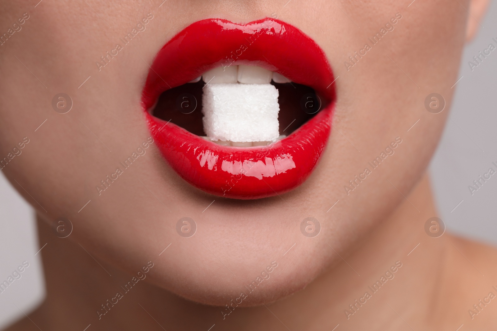 Photo of Closeup view of young woman with beautiful lips eating sugar cube on light grey background