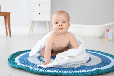 Photo of Cute little baby with soft towel on rug in bathroom