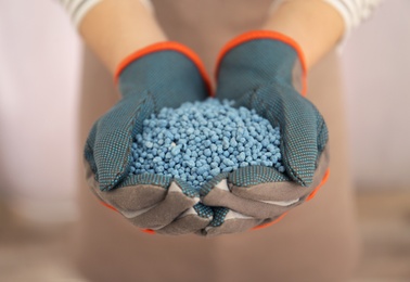 Photo of Woman holding pile of granular mineral fertilizer on light background, closeup