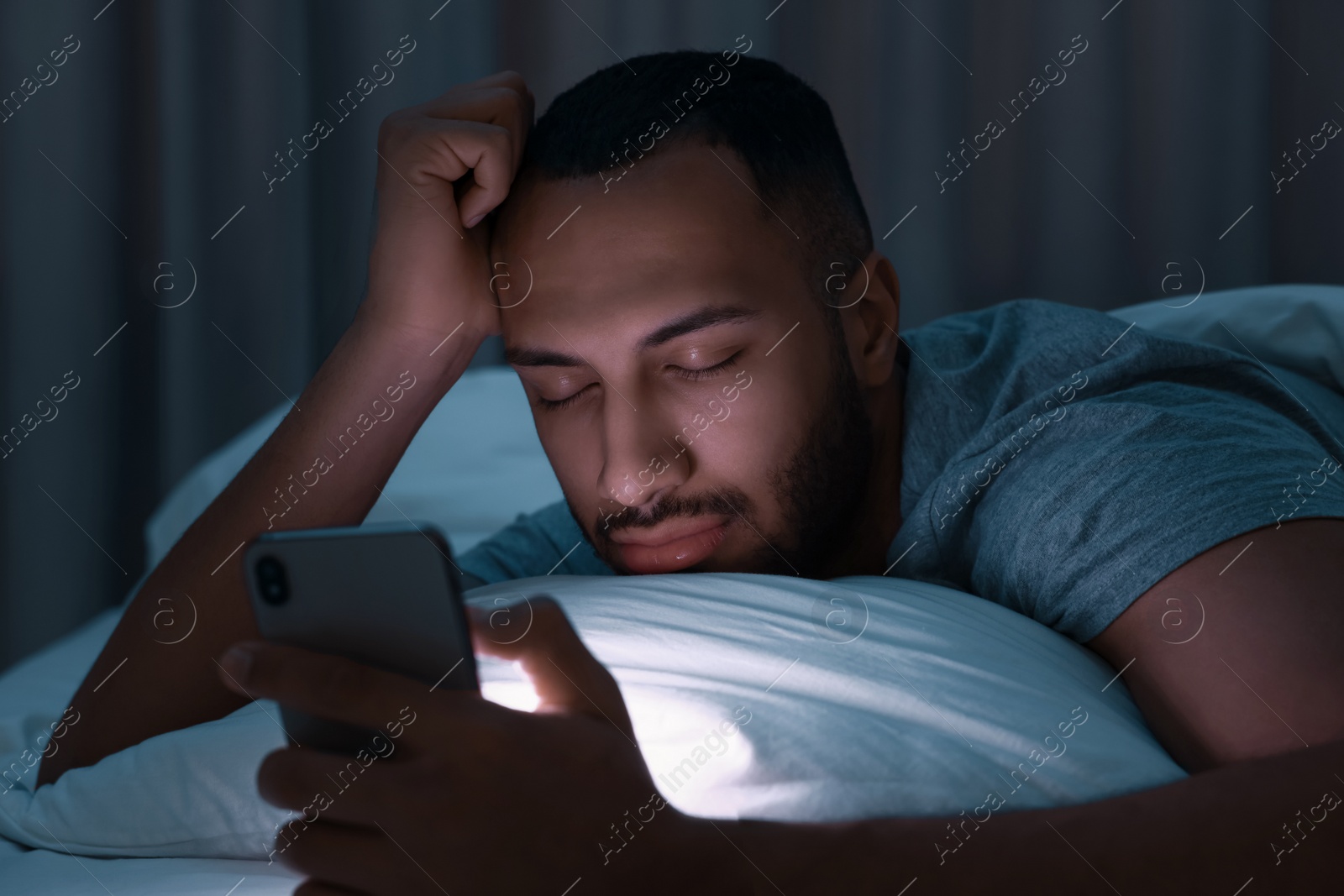 Photo of Young man sleeping while holding smartphone in bed at night. Internet addiction
