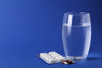 Photo of Different antidepressants and glass of water on blue background, space for text