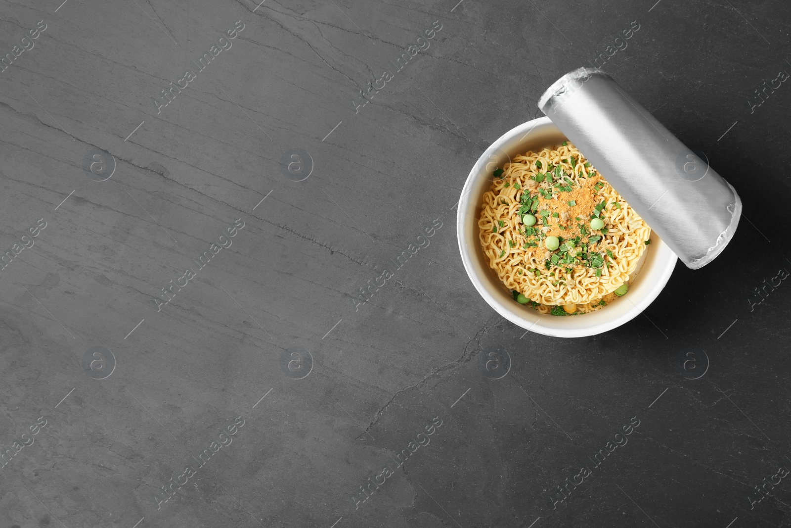 Photo of Cup of instant noodles on grey background, top view. Space for text