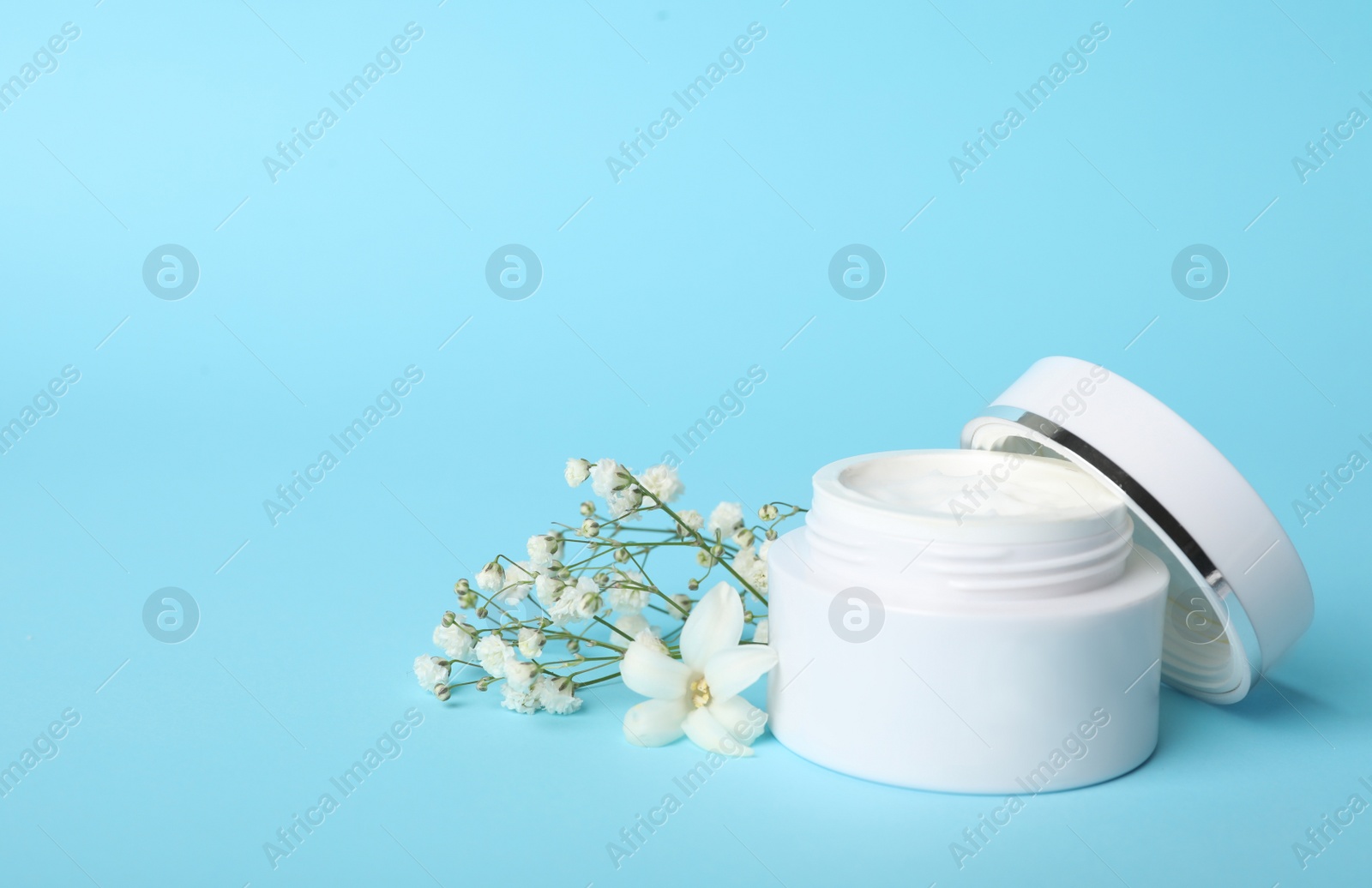 Photo of Jar of luxury face cream and flowers on light blue background. Space for text