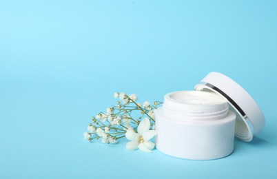 Photo of Jar of luxury face cream and flowers on light blue background. Space for text