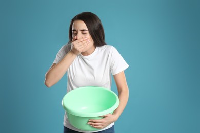 Photo of Young woman with basin suffering from nausea on light blue background. Food poisoning