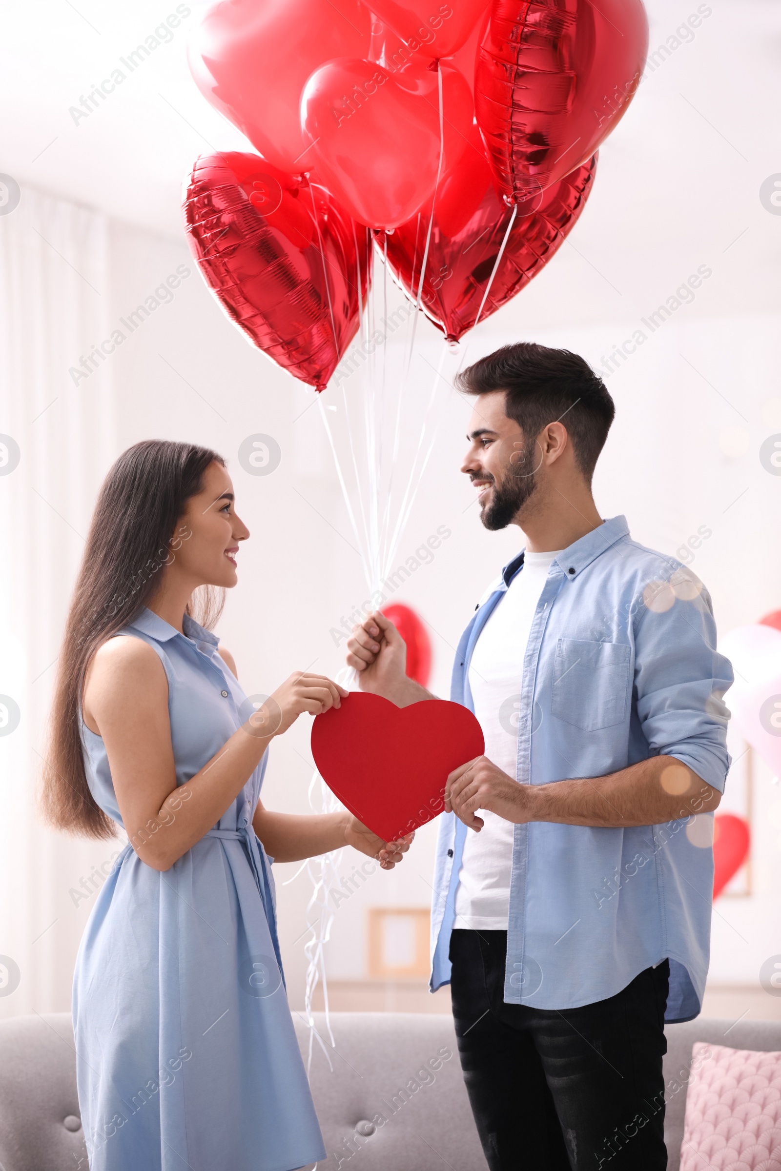 Photo of Lovely couple with heart shaped balloons in living room. Valentine's day celebration