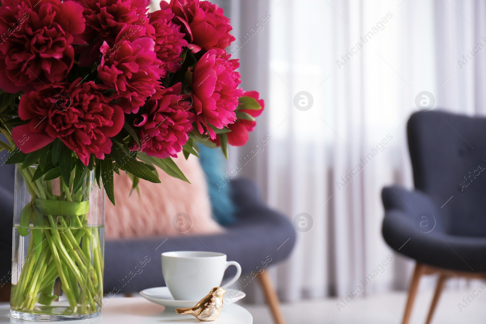 Photo of Beautiful red flowers in vase on table indoors. Interior decor element