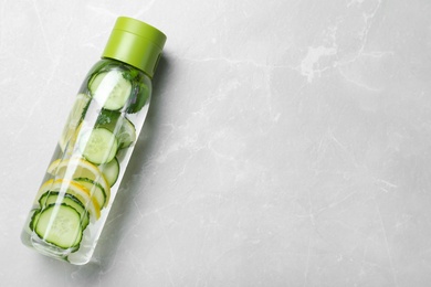 Bottle of refreshing water with cucumber, lemon and mint on light grey table, top view. Space for text