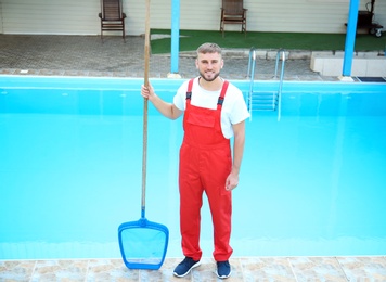 Male worker cleaning outdoor pool with scoop net