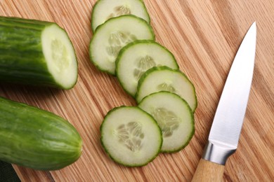 Photo of Cut cucumber and knife on wooden board, top view