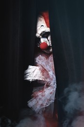 Photo of Terrifying clown hiding behind black curtains. Halloween party costume