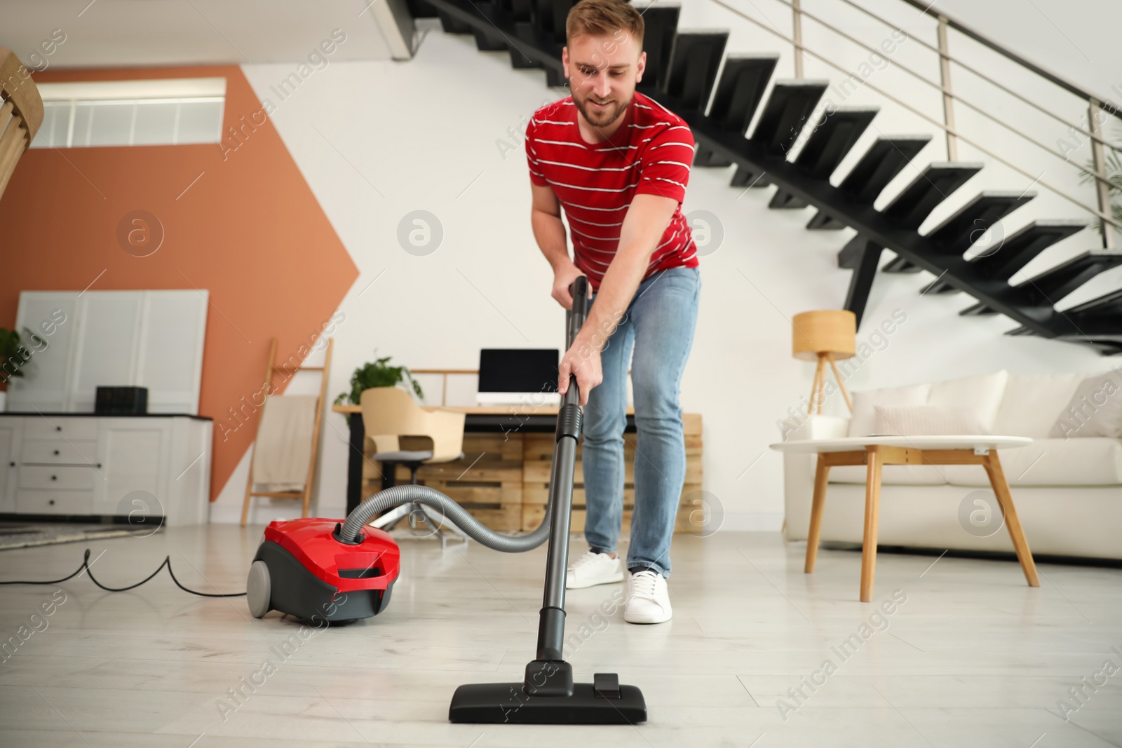 Photo of Young man using vacuum cleaner in living room