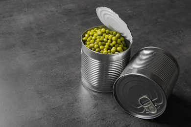 Tin cans and green peas on grey table, space for text