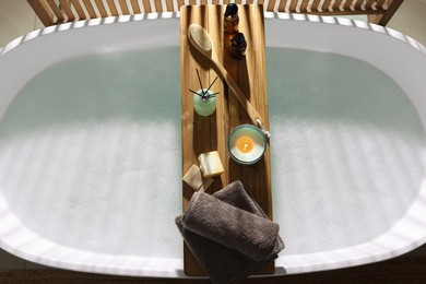 Photo of Wooden bath tray with candle and bathroom amenities on tub indoors, top view
