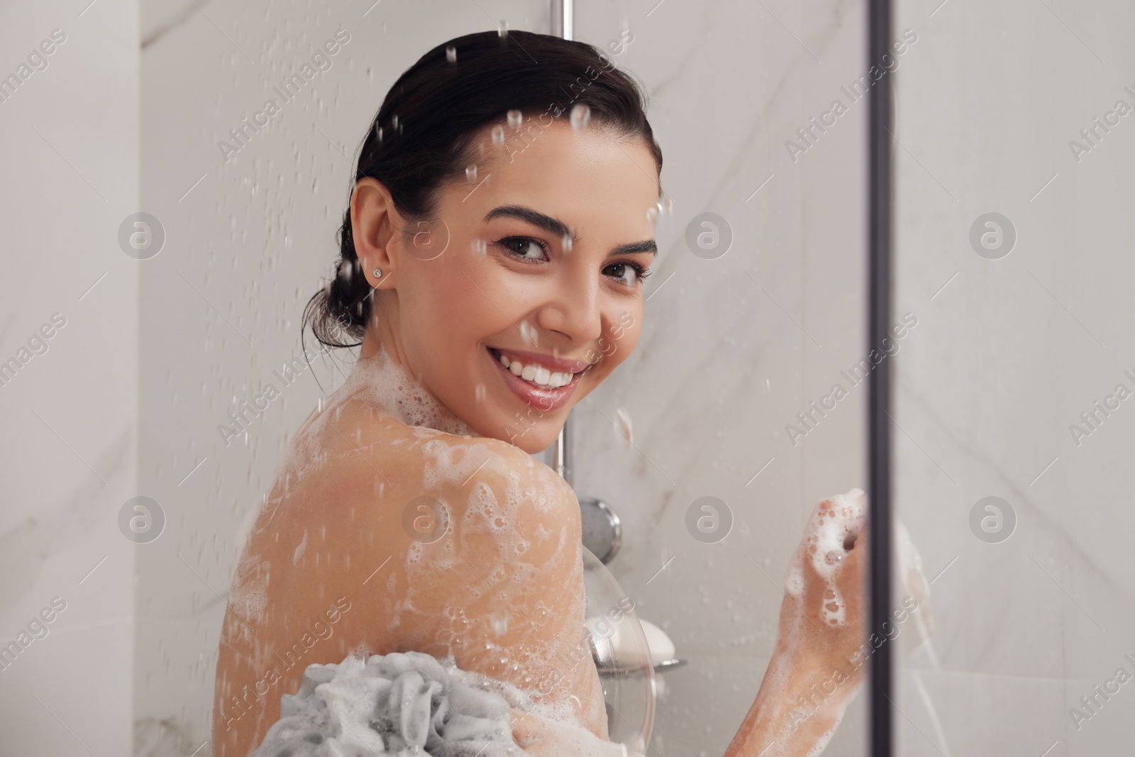 Photo of Young woman with mesh pouf taking shower at home