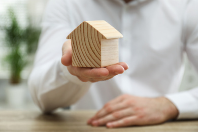 Real estate agent holding house figure indoors, closeup