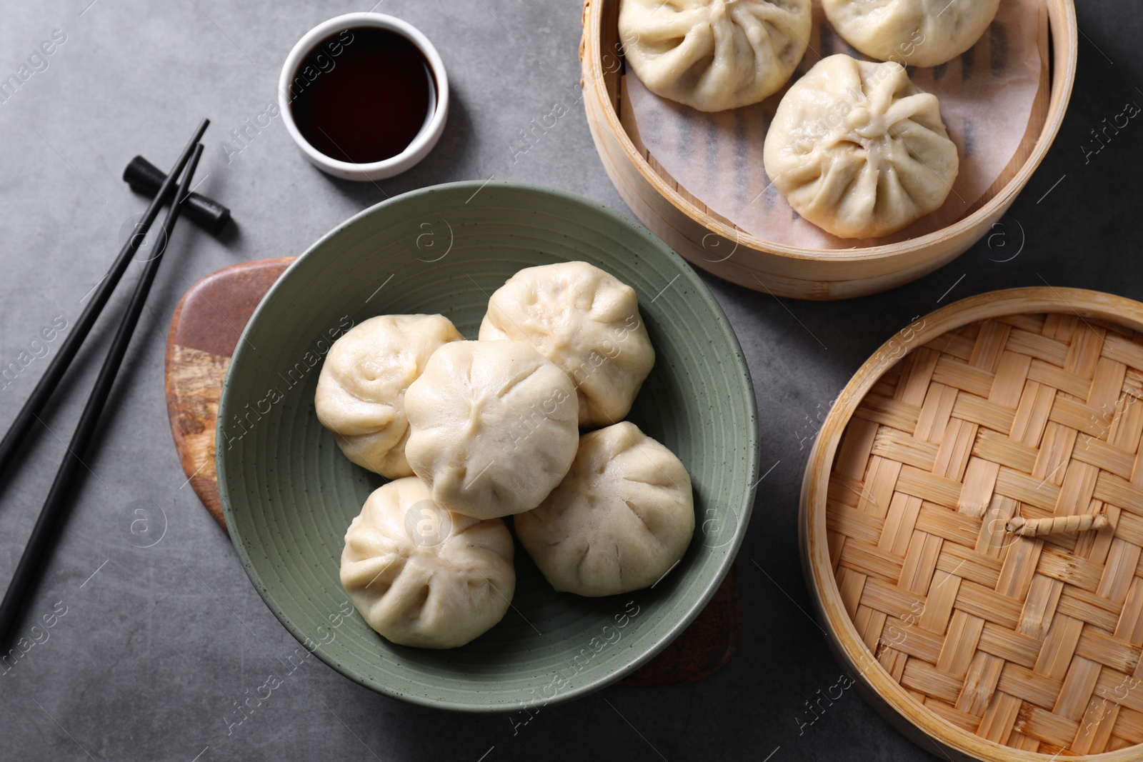 Photo of Delicious bao buns (baozi), chopsticks and soy sauce on grey table, flat lay