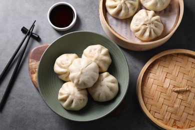 Photo of Delicious bao buns (baozi), chopsticks and soy sauce on grey table, flat lay