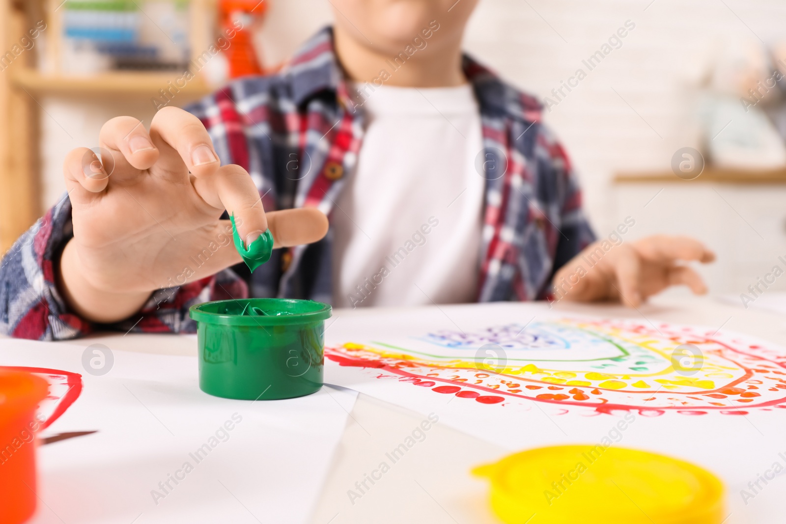 Photo of Little boy painting with finger at white table indoors, closeup