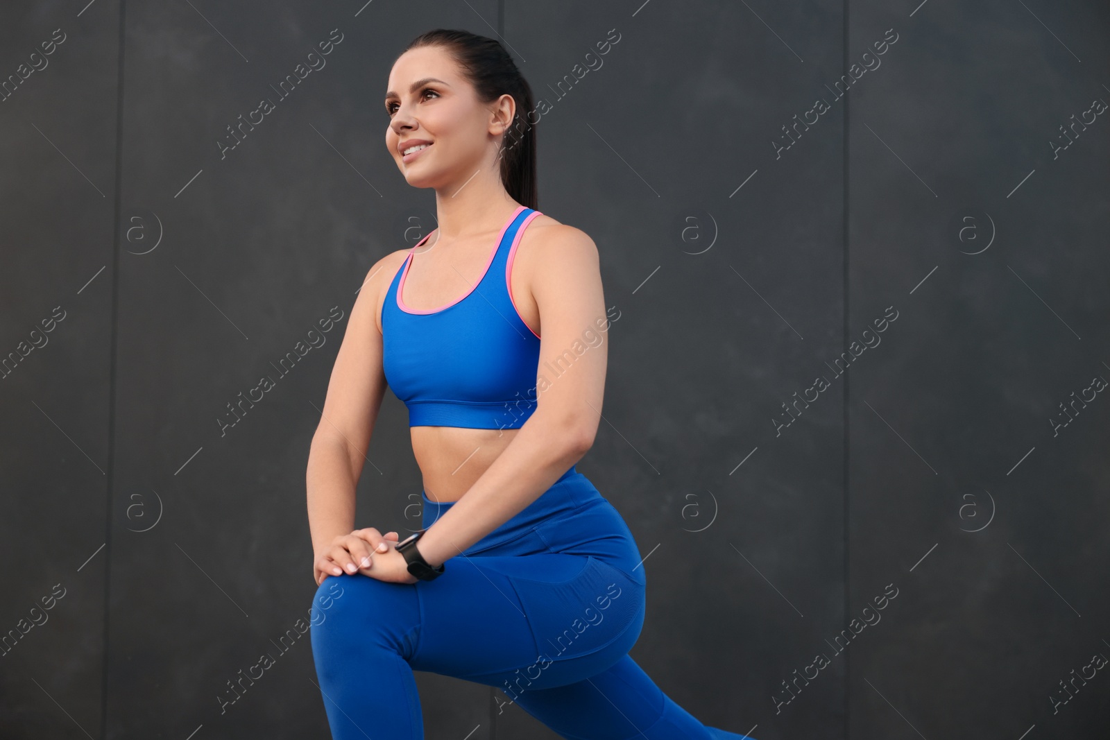 Photo of Beautiful woman in stylish sportswear doing exercises near black wall. Space for text