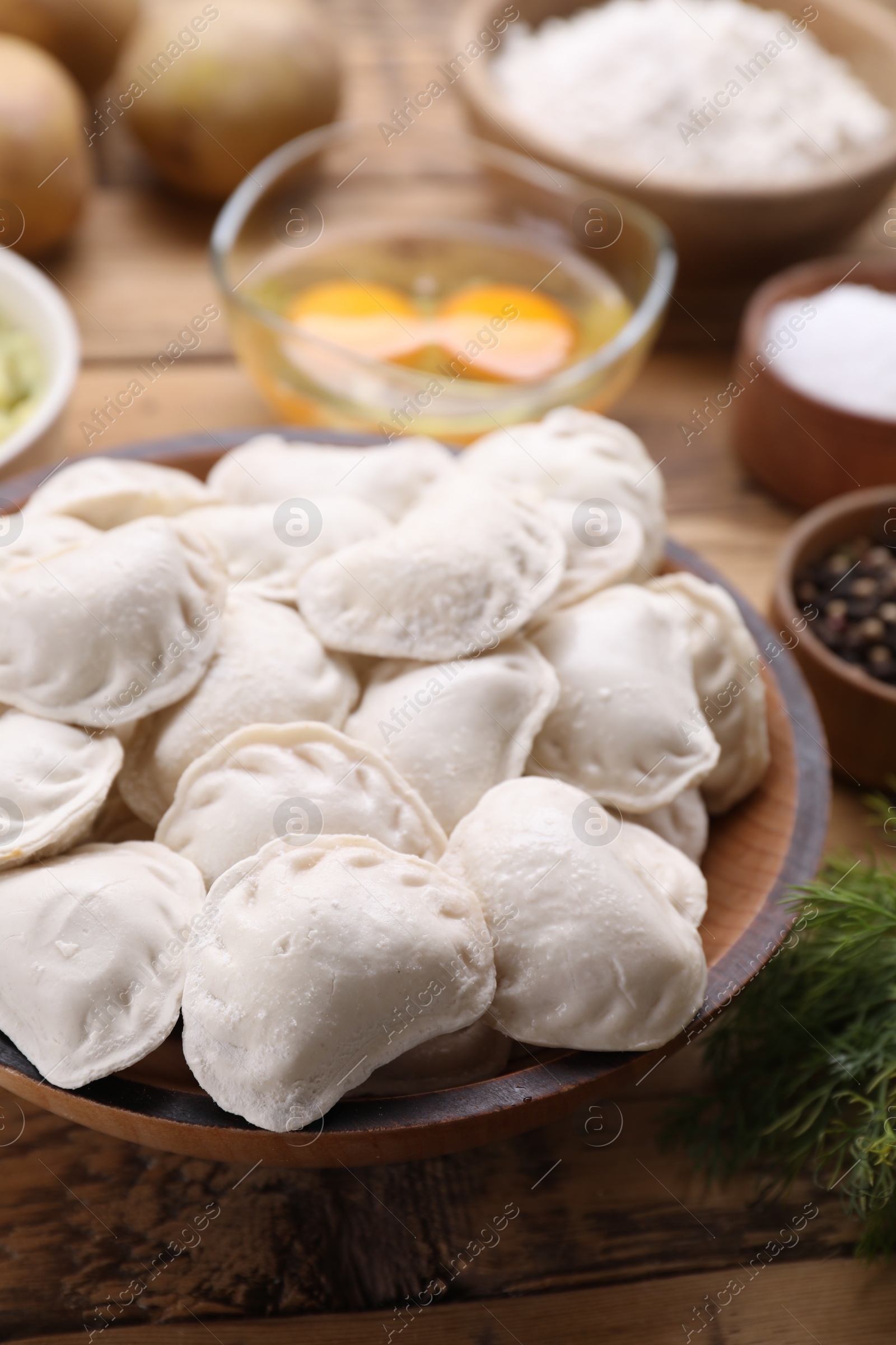 Photo of Raw dumplings (varenyky) and ingredients on wooden table, closeup