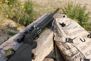 Hunting rifle and backpack on wooden bench outdoors, closeup