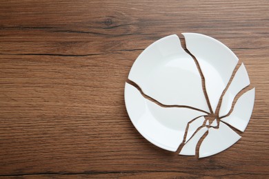 Photo of Pieces of broken ceramic plate on wooden table, flat lay. Space for text