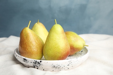 Photo of Plate with ripe juicy pears on light fabric against blue background
