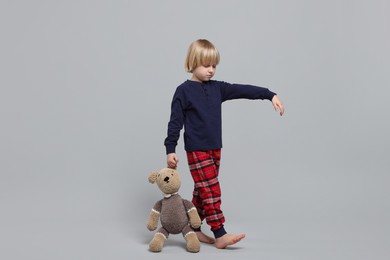 Photo of Boy in pajamas with toy bear sleepwalking on light gray background