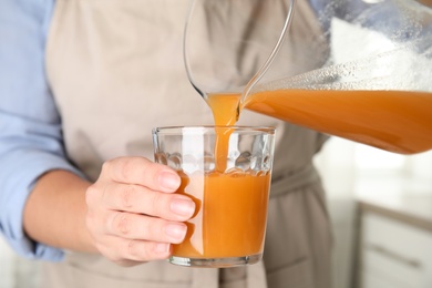 Woman pouring freshly made carrot juice into glass in kitchen, closeup