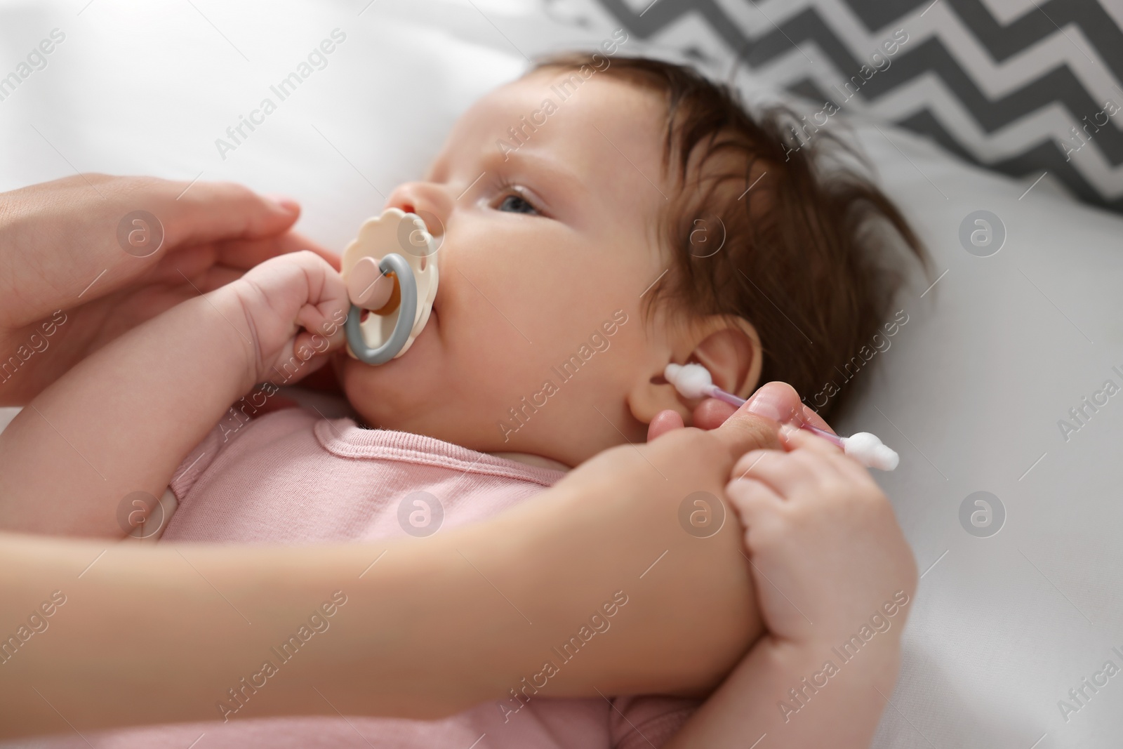 Photo of Mother cleaning ears of her baby with cotton bud on bed, closeup