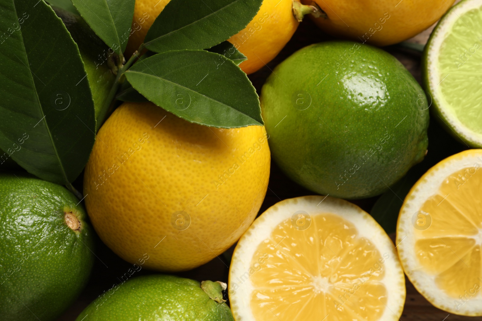 Photo of Fresh ripe lemons, limes and green leaves as background, top view