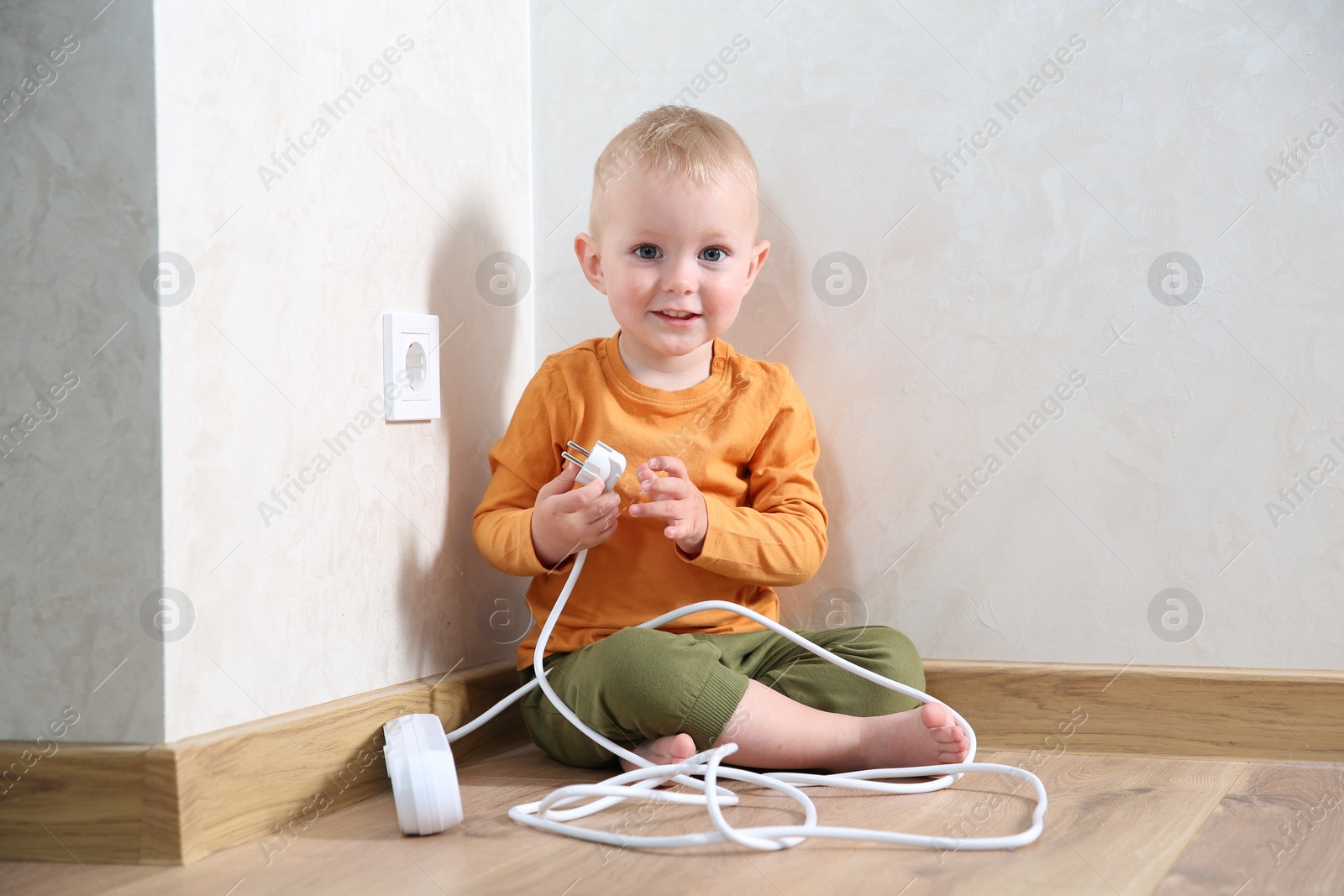 Photo of Little child playing with power strip plug near electrical socket at home. Dangerous situation