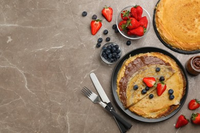 Photo of Delicious thin pancakes served with chocolate paste and berries on grey marble table, flat lay. Space for text