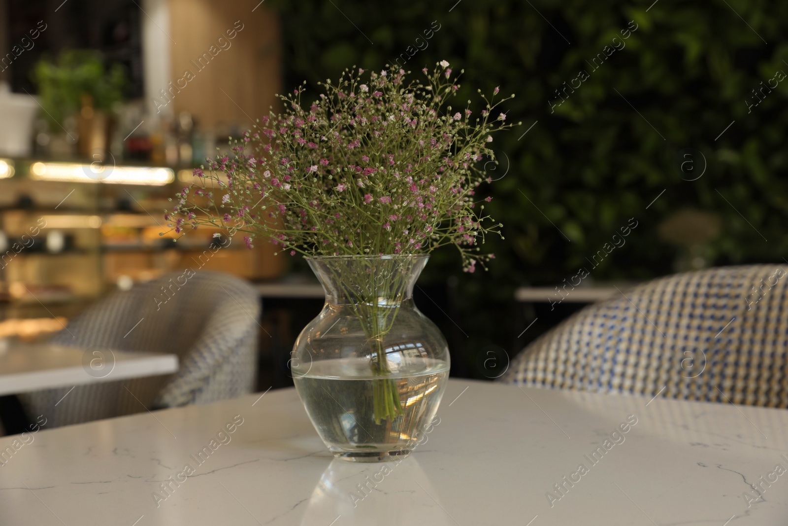 Photo of Glass vase with bouquet of beautiful flowers on table in cafe