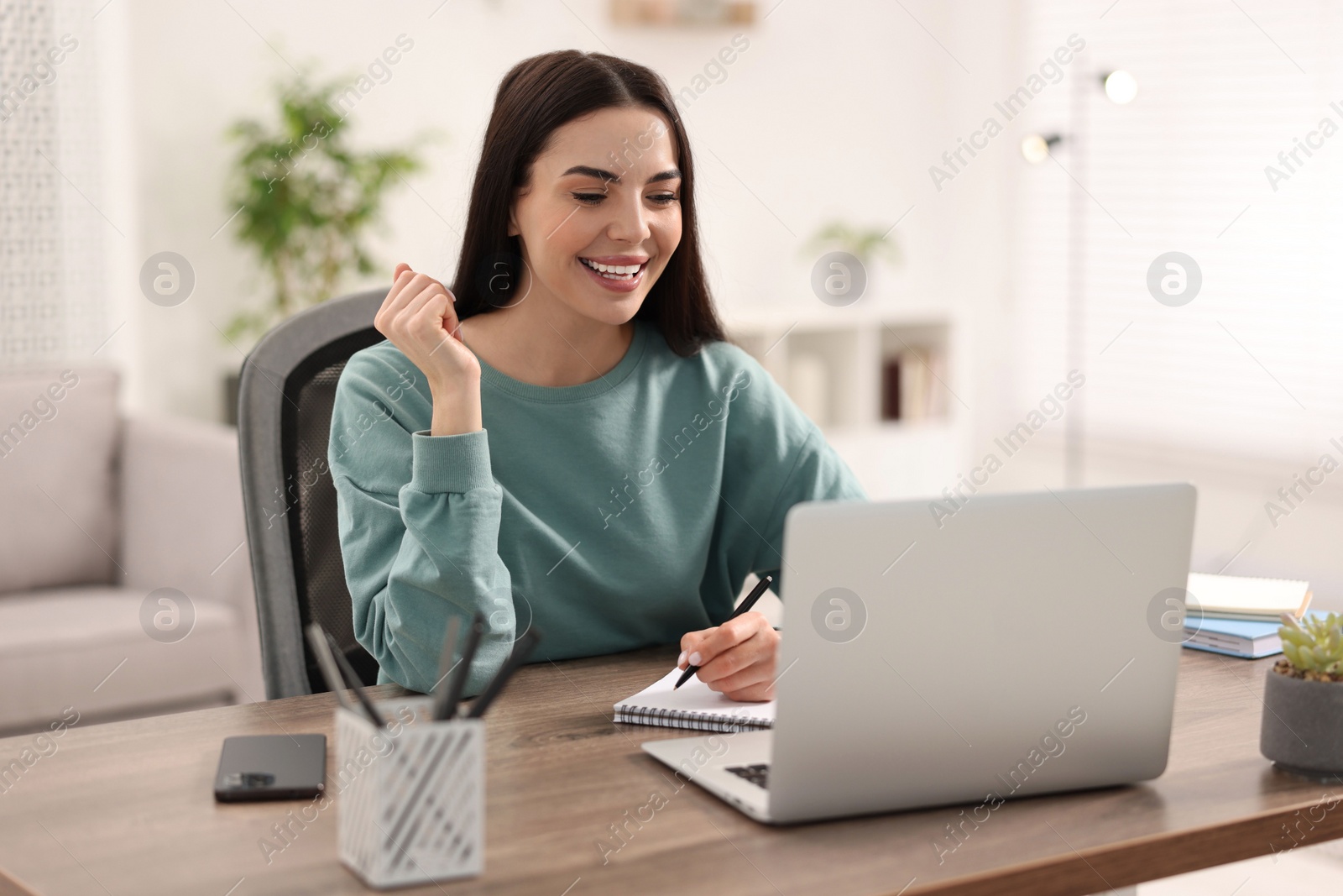 Photo of Young woman watching webinar at table in room