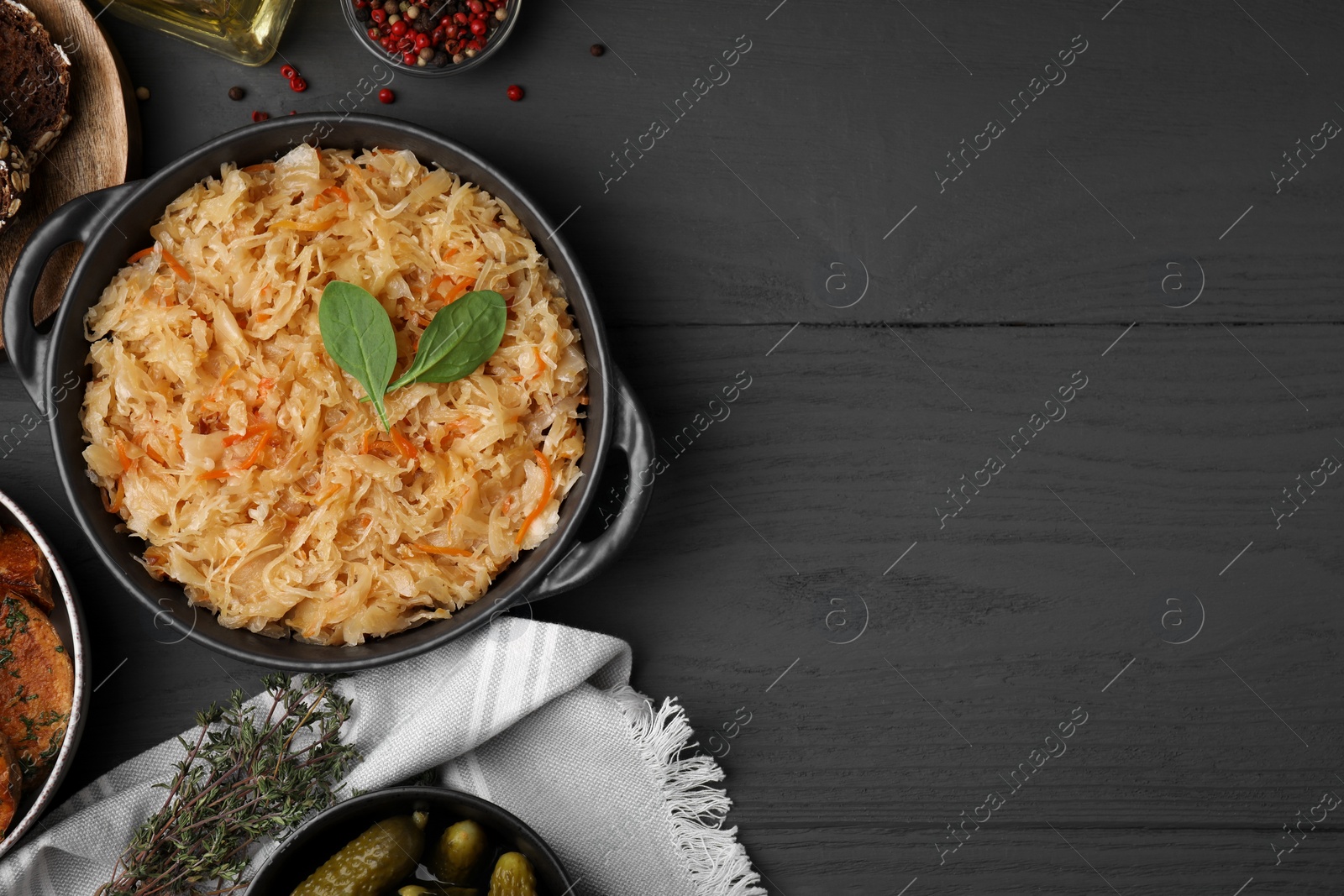 Photo of Serving pan with sauerkraut and products on black wooden table, flat lay. Space for text