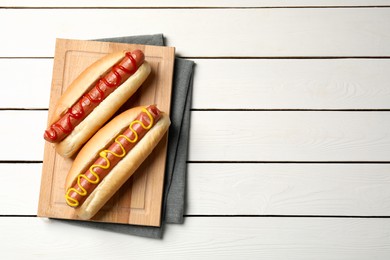 Photo of Delicious hot dogs with mustard and ketchup on white wooden table, top view. Space for text