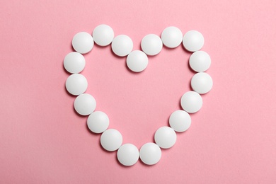 Heart made with white pills on color background